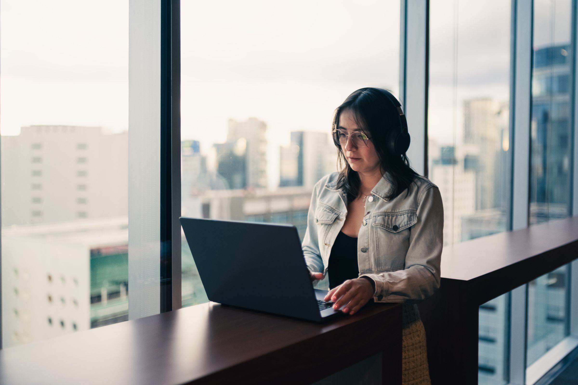 Professional working through her CRM pipeline on a laptop beside a city-view window