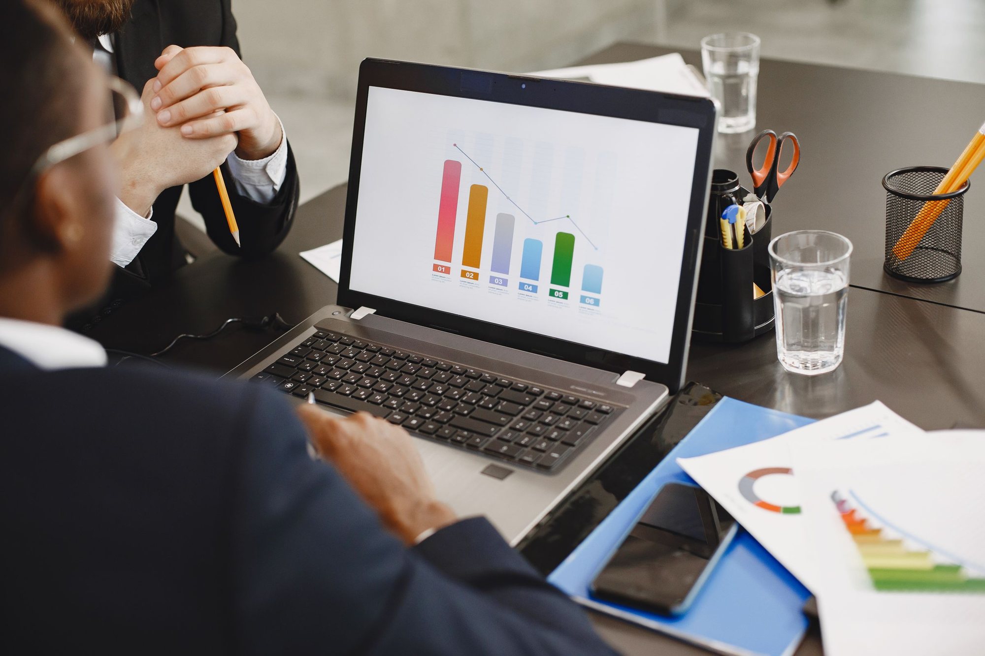 Laptop showing a bar chart on a desk beside printed reports